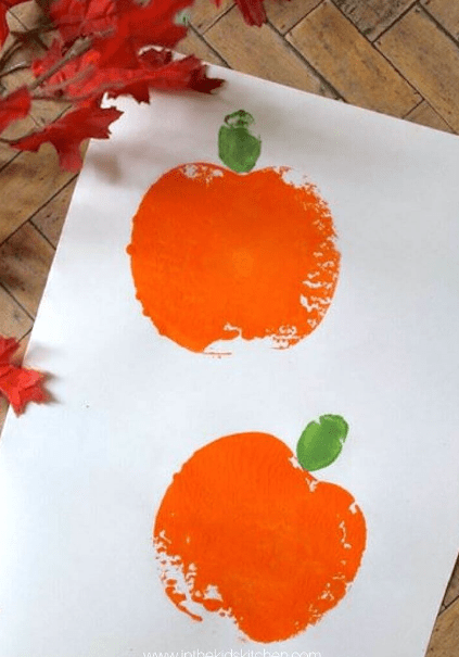 fall art activity shows two pumpkins painted by stamping apples.