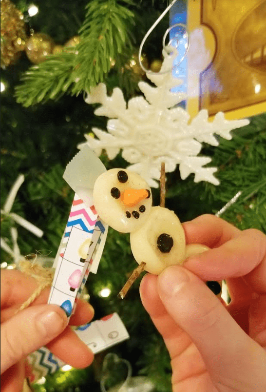 Christmas crafts for kids shows a snowman craft on a tree with a piece of paper stuck to the back.