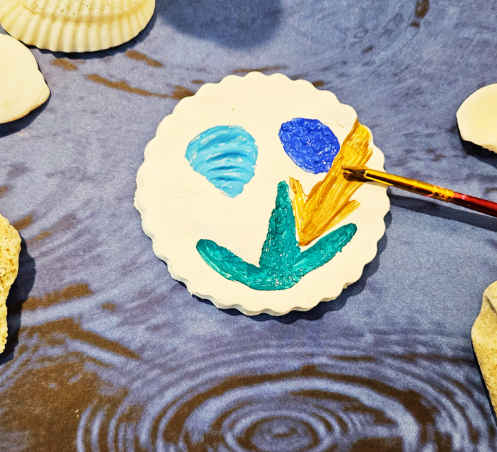 nature art shows a circle piece of play with three shell prints and it is being painted.