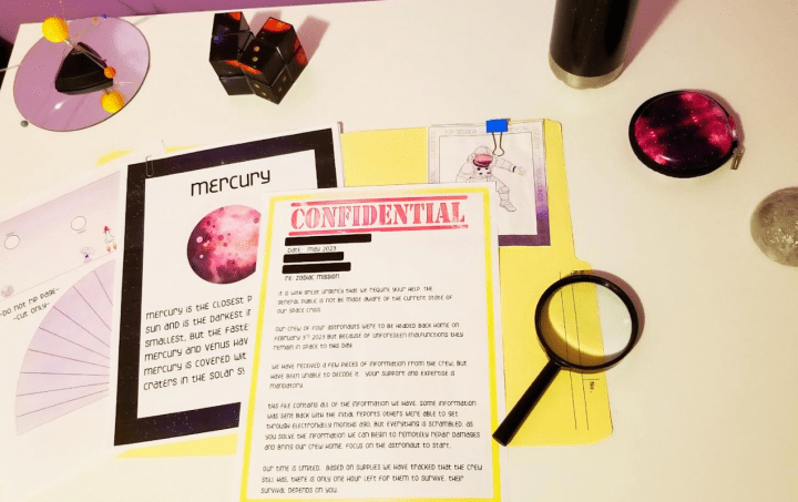 escape room challenge shows pages, magnifying glass and space items on a desk.