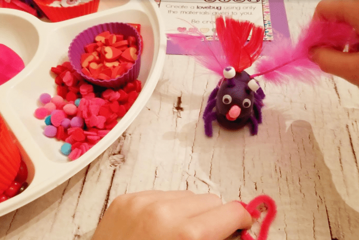 valentines stem activity shows a child creating a lovebug with purple play and small beads.