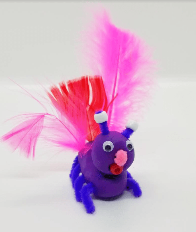 valentines day stem for kids shows a purple critter made from clay with pipcleaner legs and feathers.