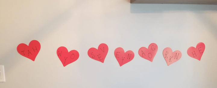 valentines day escape room shows seven hearts taped to the wall with letters on each.