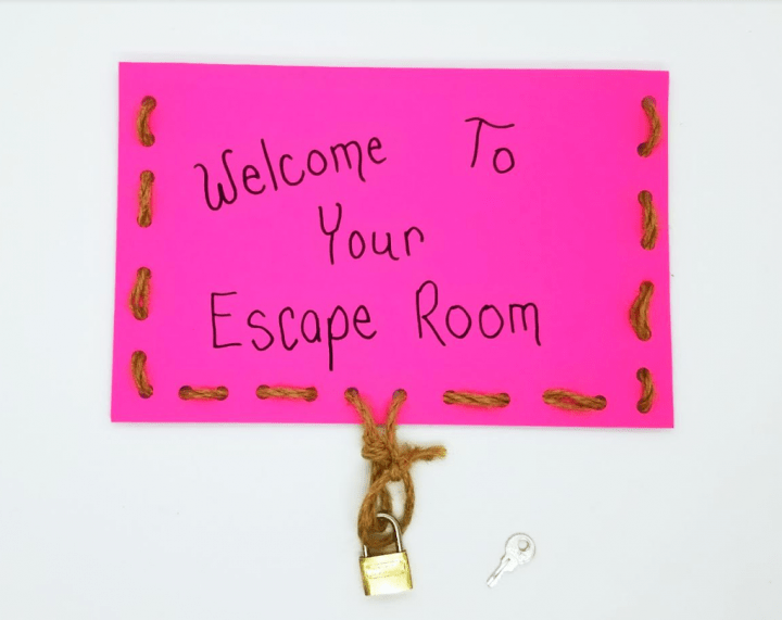 escape room clues shows a folded paper with string weaved around the sides and locked at the front with the words welcome to your escape room on the front.