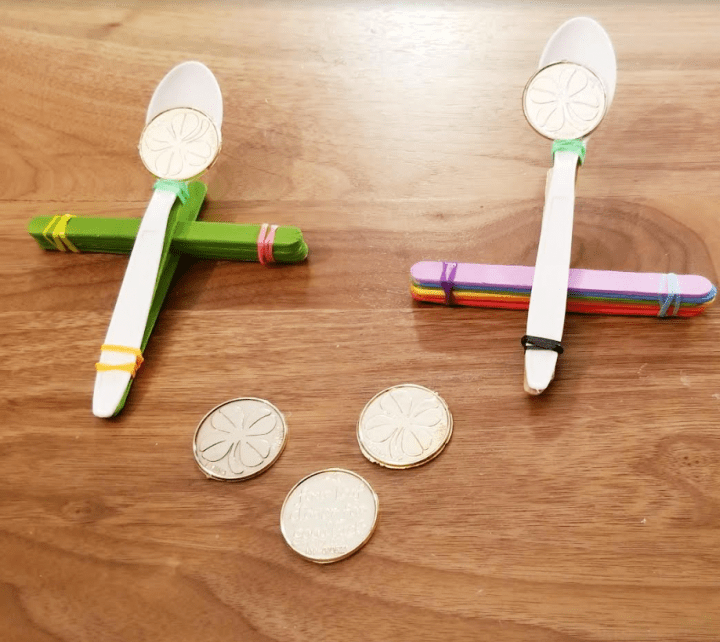 st. patricks day stem challenge shows two catapults on a table with plastic gold coins on each.
