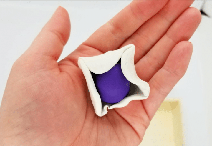 escape room puzzles shows a hand holding a purple ball of clay being wrapped with white clay.