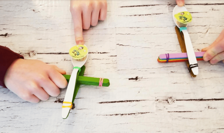 st. patricks day stem challenge shows two children holding onto their DIY catapults.