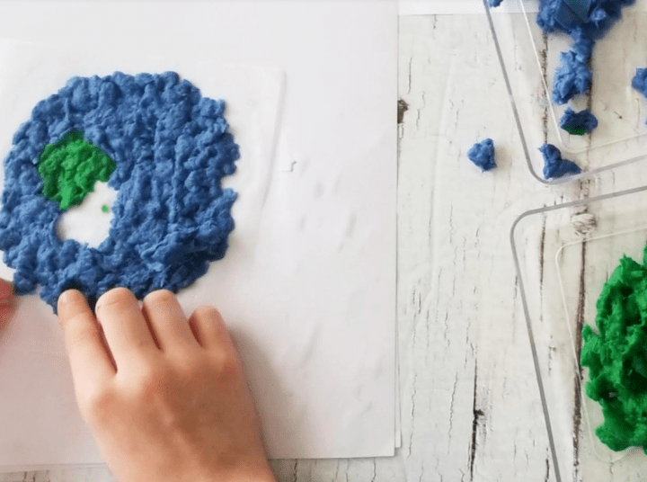 Earth Day activity shows a child placing blue paper pulp on a sheet of paper.