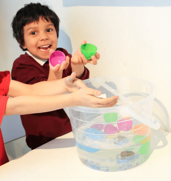 EAster stem shows a child who looks excited as he opens a plastic egg from a bucket of water.