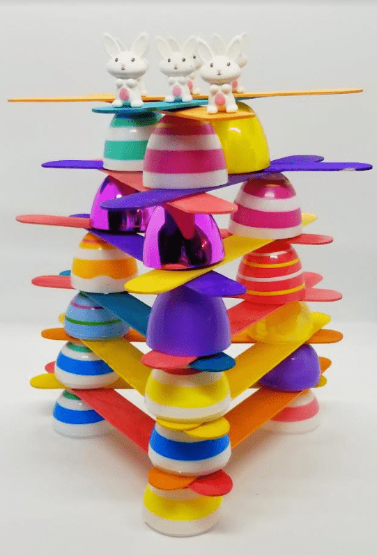 Easter STEM activity for kids shows a structure made from eggs and popsicle sticks with bunnies on top.