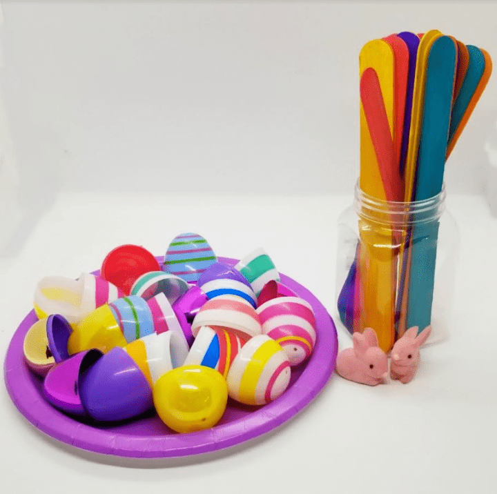 Easter stem activity shows a container of tongue depressors and a plate with plastic Easter eggs on it and little pink bunny figures.