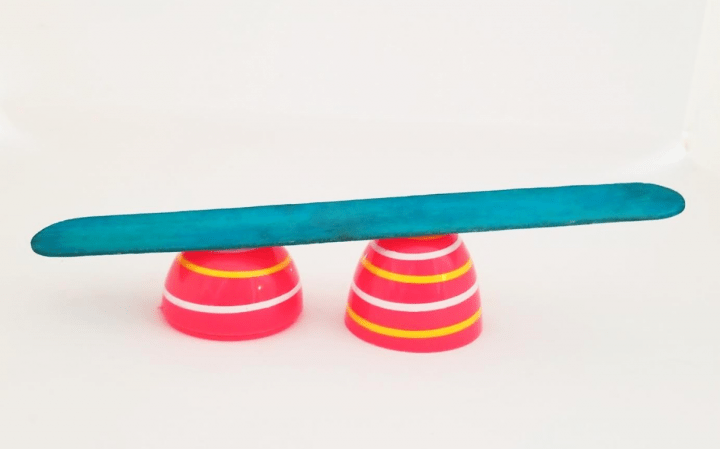 STEM challenge for kids shows two plastic Easter egg halves with a popsicle stick across the top of them.