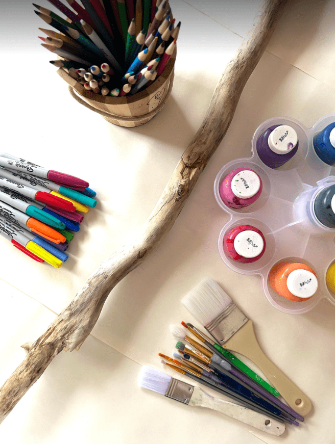 art for kids shows a stick and containers with crayons, paint and brushes.