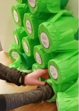 escape game puzzle ideas shows a child poking through a green tissue paper cylinder tree.