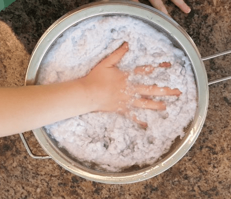 recycled crafts shows a child squishing paper pulp through a strainer.