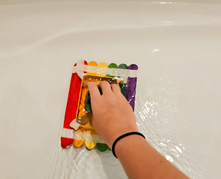 building challenge shows a child pushing down a popsicle stick boat into water.
