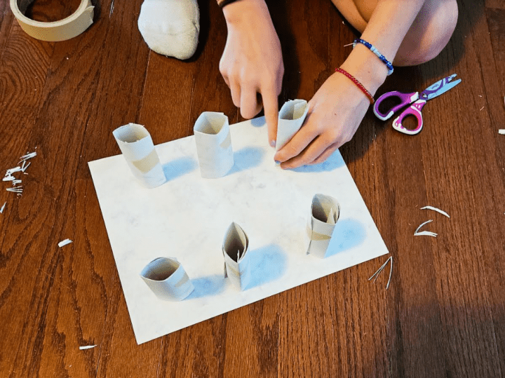 STEM challenge shows a child building six paper rolls stuck to a page.