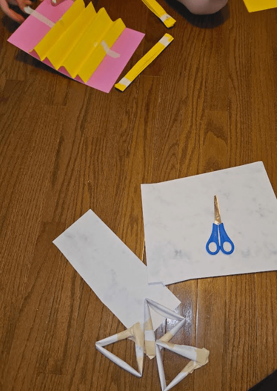 STEM challenge shows children creating a cutting paper on a floor.