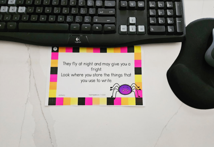 free classroom halloween scavenger hunt shows a riddle printed on paper on a desk with a computer keybaord.