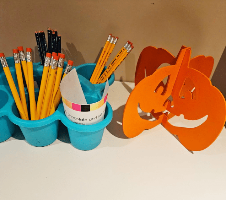 free classroom halloween scavenger hunt shows a container with pencils and a pumpkin decoration.
