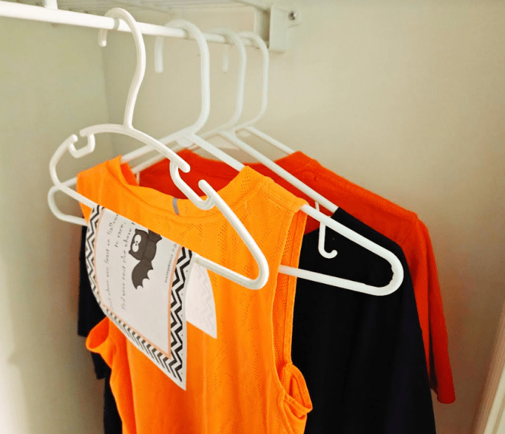 halloween activity for kids shows orange and black clothes hanging in a closet with a printed clue hanging.