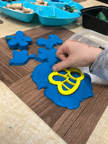 technology for kids shows a child putting a bee cookie cutter in blue playdough.