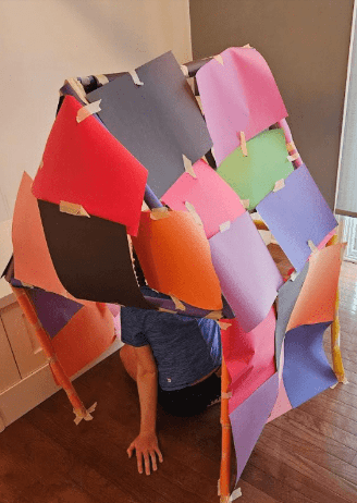 best stem activities for kids shows a house made from paper and tape that a child is sitting in.