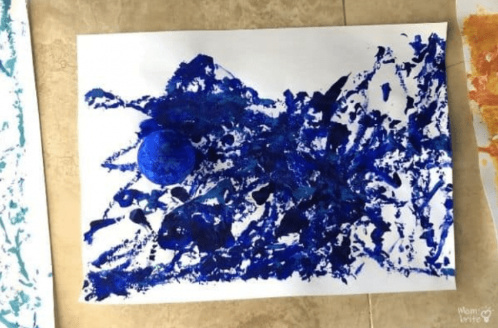space art project for kids shows a blue sheet of paper with a marble rolled all over it.