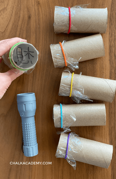science experiments for kids shows six toilet rolls with elastics and a clear film on the end with letters.