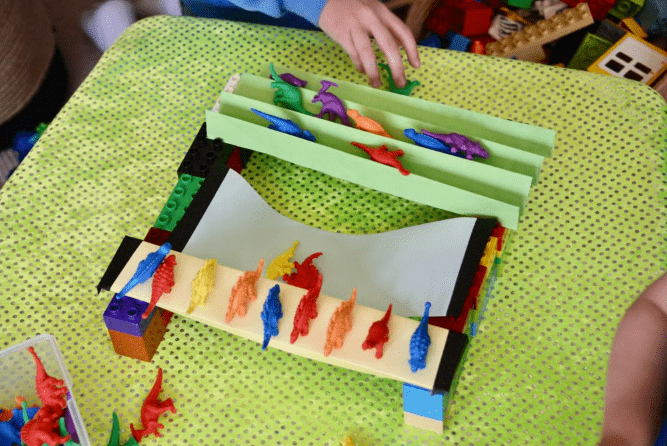 bridge building stem challenge shows a paper bridge with plastic dino figures on it.