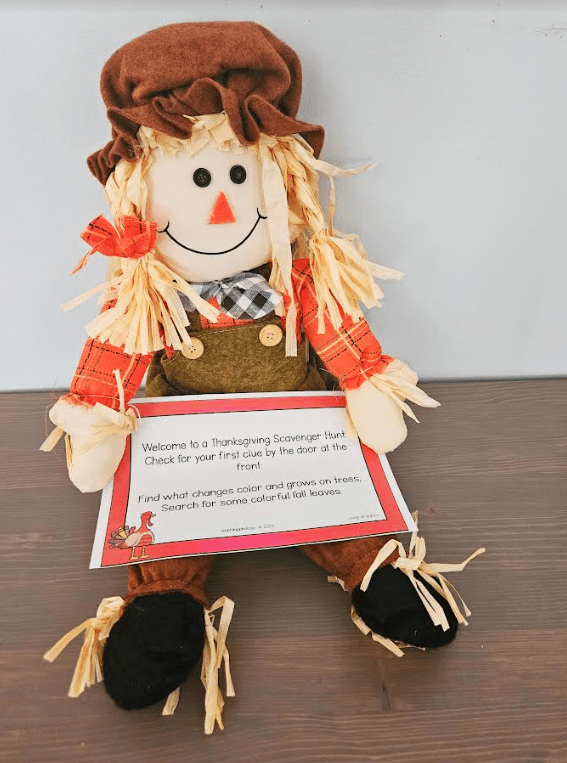 free Thanksgiving classroom scavenger hunt shows a scarecrow toy with a scavenger hunt clue on its lap.