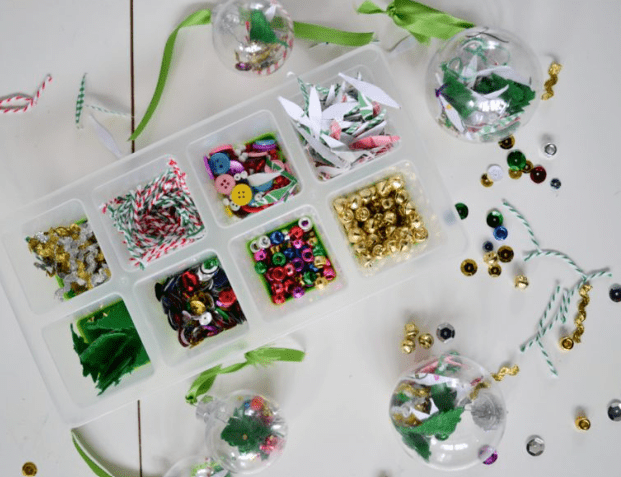 preschool christmas craft shows a container with beads and other things to put inside a christmas ornament.
