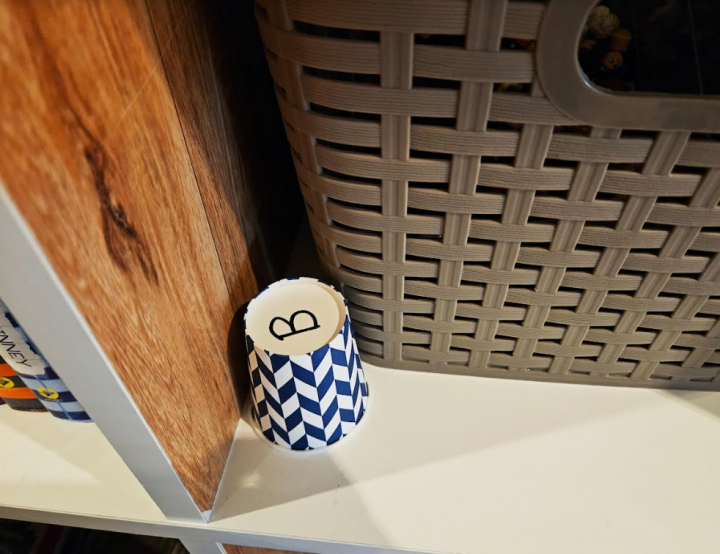DIY escape room shows a cup with the letter B written on the bottom and set in a shelf.