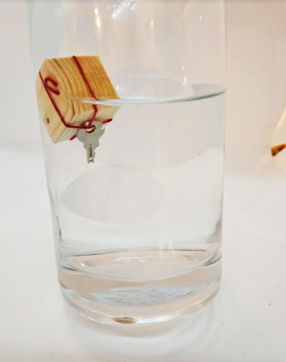 escape room ideas shows a key floating in a jar attached to a wooden cube.