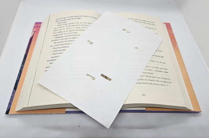 diy escape room at home shows a book with another sheet of paper on top with slits cut into it.