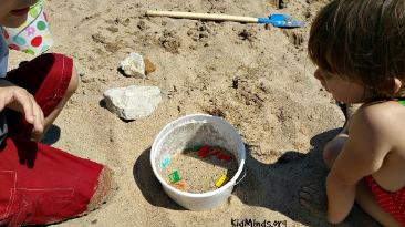 outdoor science for kids shows two children on the beach looking at a bucket with sand and lego.