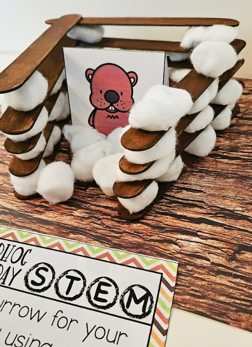 free groundhog day STEM activity shows a printed image of a groundhog inside a structure made from cotton balls and popsicle sticks.