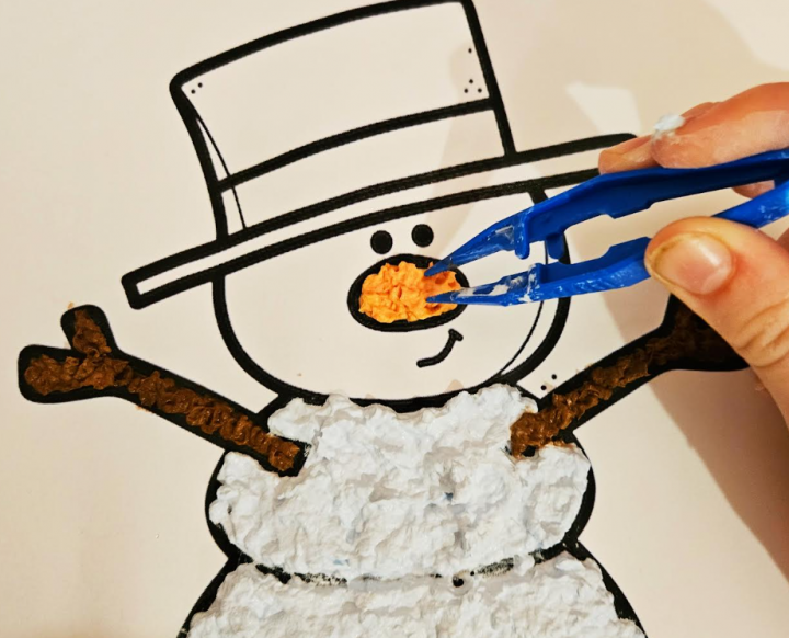 winter paper mache art for kids shows a snowman's nose being added with a piece of paper mache.