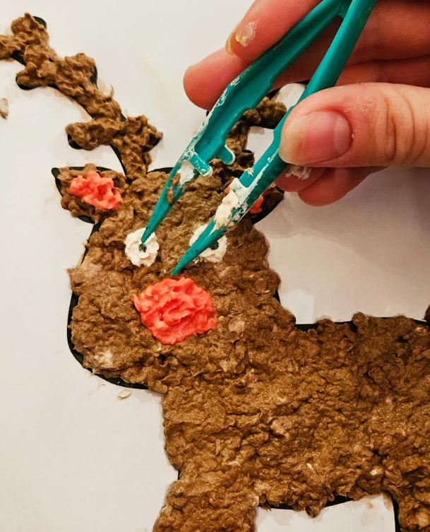 free paper mache reindeer template is shown with someone using tweezers placing some of the paper pulp into place.