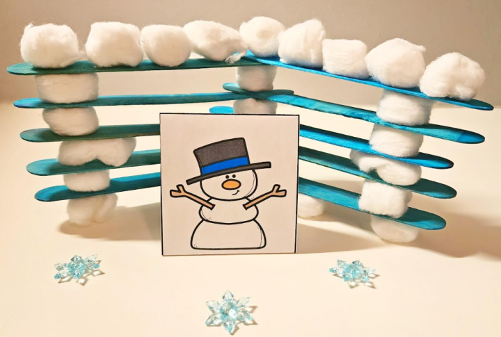 free winter STEM activity shows a wall made from popsicle sticks and cotton balls with a snowman figure standing out front.