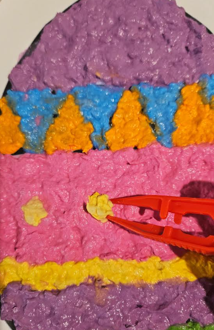 messy craft for kids shows a child using a tweezer to place pieces of paper mache onto an egg.