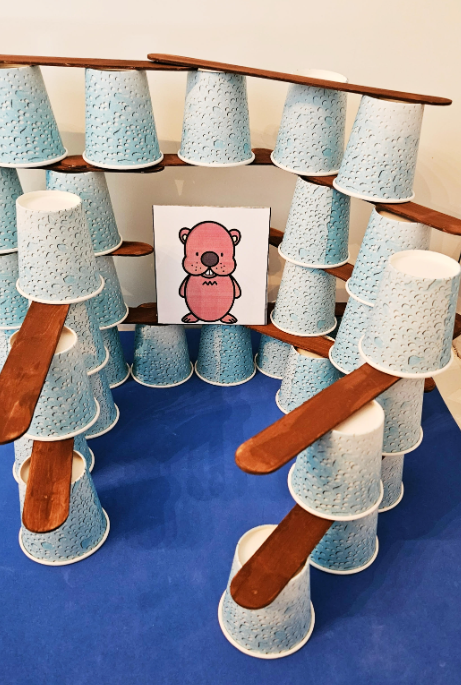 kindergarten activities for kids shows a groundhog inside of a structure made from ups and sticks.