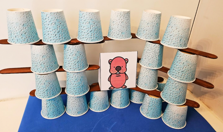 free groundhog day STEM shows a printed picture of a groundhog surrounded by a structure made from dixie cups and popsicle sticks.