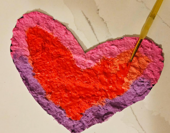 messy art for kids shows a child painting red onto a paper mache heart.