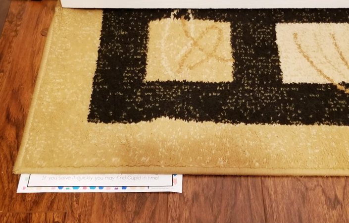 Valentines escape room for kids shows a folded up clue hidden under a rug.